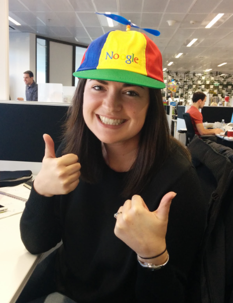 Meg Smith wearing a Noogler hat, a big smile and two thumbs up.